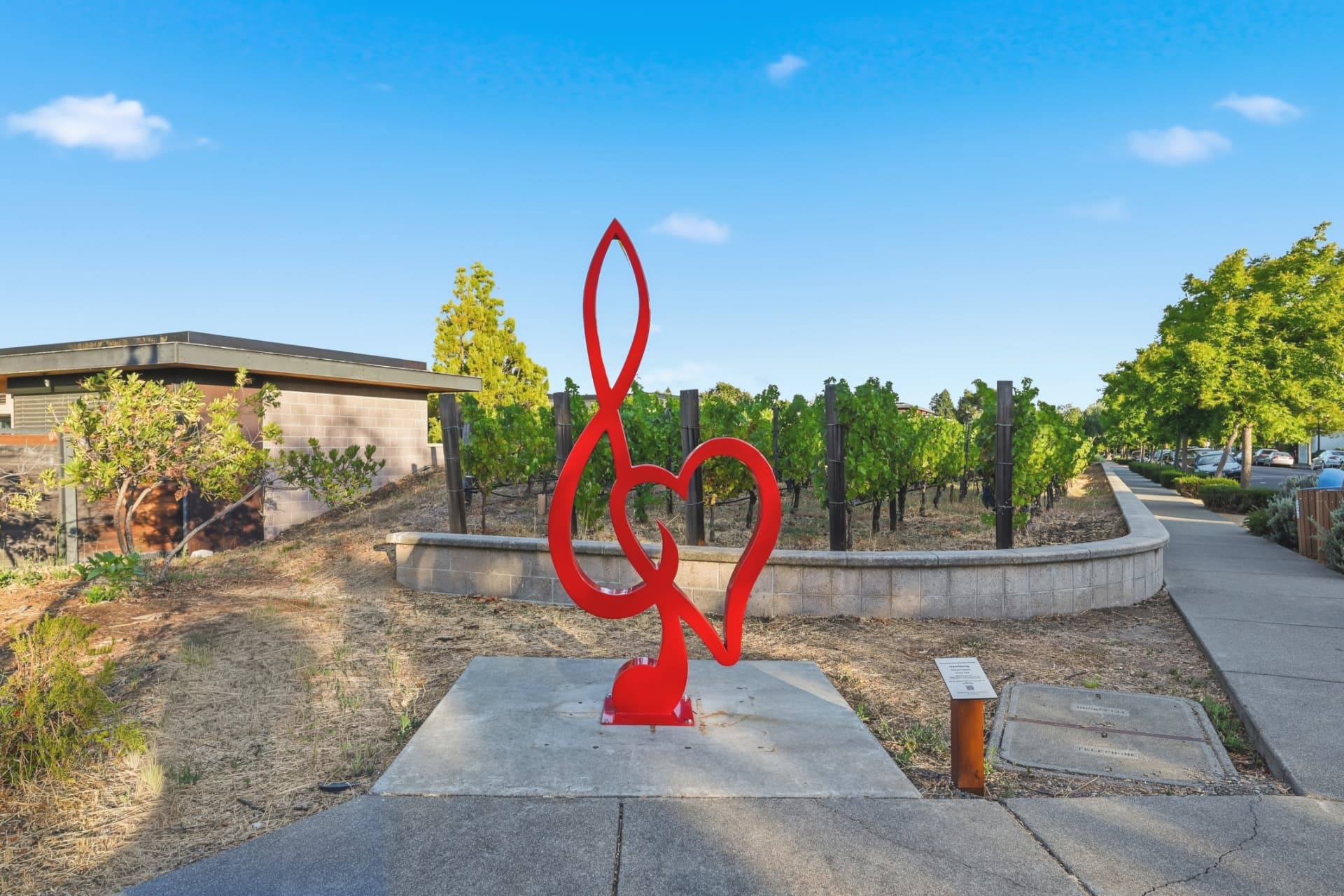 Red heart sculpture beside vineyard rows along a Yountville sidewalk